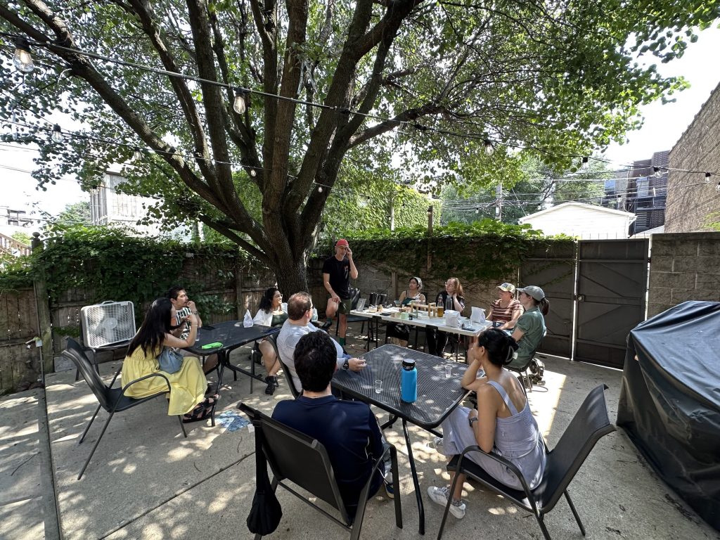 Chicago Matcha Club members seated around tables on a string-lit patio under a tree at the first meetup, July 2025