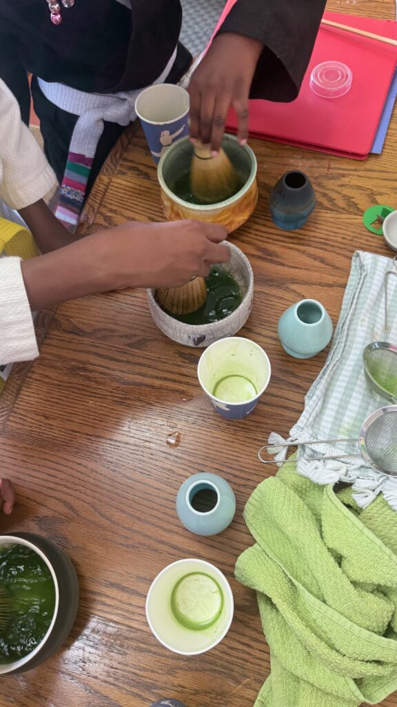 Two young participants whisking their own bowls of matcha at a wooden table